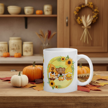 Load image into Gallery viewer, White mug with a colorful design featuring sunflowers and pumpkins on a wooden table with fall decorations.