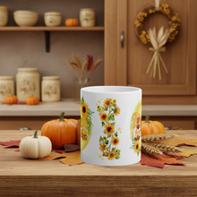 Load image into Gallery viewer, White mug with sunflower design on a wooden table with pumpkins and fall decorations.