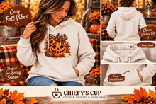 Load image into Gallery viewer, A woman wearing a cream-colored hoodie with a pumpkin graphic, shown in a cozy autumn-themed setting alongside product feature callouts and a brand logo for Chiefy's Cup.