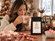 Load image into Gallery viewer, A woman in a cozy knit sweater sits at a wooden table, holding a mug with a red snowflake design. In front of her is a bag of Chiefy's Cup Coffee, specifically Frosted Peppermint Growing Coffee, surrounded by holiday decorations like cookies, candy canes, and a bowl of pink peppermint candies.