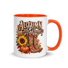 Load image into Gallery viewer, A white ceramic coffee mug with a bright orange handle and interior, featuring a western-themed autumn graphic with the text 'Autumn on the Range' above cowboy boots, pumpkins, sunflowers, and fall leaves.