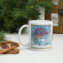 Load image into Gallery viewer, Left Side view of a white glossy mug with the phrase "Merry Christmas," featuring a design of a cute car carrying a Christmas tree through snow, with a sparkly golden frame and festive blue hue background.