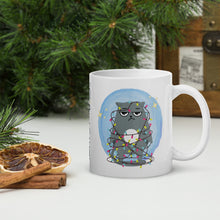 Load image into Gallery viewer, Right side view of a white glossy mug with an image design of a sad kitten tangled in Christmas lights, surrounded by golden sparkles, with a soft blue hue circle background.