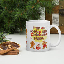Load image into Gallery viewer, Right side view of a white glossy mug with the phrase "I run on coffee and Christmas cheer" in festive font, featuring a Christmas mug topped with whipped cream, gingerbread men and women, with sparkles and a yellow mist in the background.