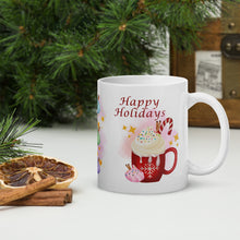Load image into Gallery viewer, Right side view of a white glossy mug featuring the phrase "Happy Holidays" with a festive red mug design, topped with whipped cream, candy cane, cinnamon sticks, sprinkles, and golden sparkles, set against a pink-hued background.