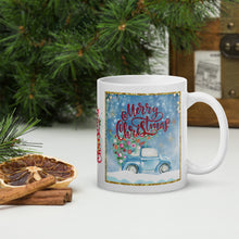 Load image into Gallery viewer, Right Side view of a white glossy mug with the phrase "Merry Christmas," featuring a design of a cute car carrying a Christmas tree through snow, with a sparkly golden frame and festive blue hue background.