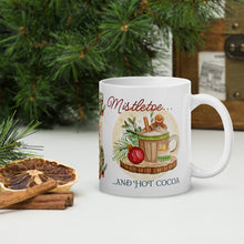Load image into Gallery viewer, Right side view of a white glossy mug with the phrase "Mistletoe and Hot Cocoa" in festive font, featuring a design of a Christmas cup with a gingerbread man, whipped cream, ornaments, mistletoe, pine trimmings, and golden sparkles, with a round brown circle in the background.
