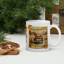 Load image into Gallery viewer, Right side view of a white glossy mug with the phrase "Thankful and Blessed" in festive font, featuring an image of an old truck on a country road with a bed full of pumpkins on a late autumn day with a festive frame.