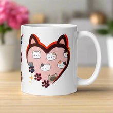Load image into Gallery viewer, Right side view of a white glossy mug with a heart frame featuring cat ears on top of the heart. Inside the frame are cute cat faces surrounded by golden sparkles. On the side of the frame, there is one small pink, one blue, and one purple paw print.