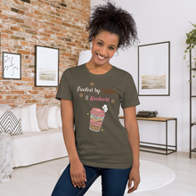 Load image into Gallery viewer, Woman wearing a t-shirt with &#39;Fueled by Coffee &amp; Kindness&#39; design in a cozy living room.
