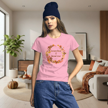 Load image into Gallery viewer, Woman wearing a pink t-shirt with a floral design and text in a living room.

