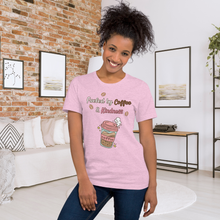 Load image into Gallery viewer, Woman wearing a pink t-shirt with coffee-themed design in a cozy living room.
