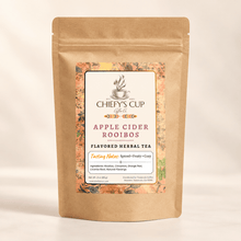 Load image into Gallery viewer, A kraft paper stand-up pouch of Chiefy's Cup Tea Co. Apple Cider Rooibos Flavored Herbal Tea, featuring a central white label with orange and green accents, set against a warm beige background.
