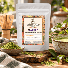 Load image into Gallery viewer, A stand-up pouch of Chiefy's Cup Matcha green tea powder stands on a wooden surface, surrounded by matcha powder in a bowl, a cup of matcha tea, leaves, and a bamboo whisk in a styled kitchen setting.
