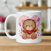 Load image into Gallery viewer, Left side view of a white glossy mug featuring a cute teddy bear holding a string of red hearts, with pink hearts surrounding the bear, golden sparkles in the background, and a large pink heart behind the bear.
