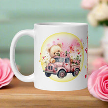 Load image into Gallery viewer, Left-side view of a white glossy mug featuring a cute bear in an old red truck with pink roses in the truck bed, surrounded by pink and red hearts, golden glitter, and a yellow circle.
