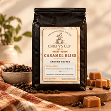 Load image into Gallery viewer, A black bag of Chiefy's Cup Coffee Co. Caramel Bliss ground coffee stands on a wooden surface with coffee beans, caramel cubes, and a warm blurred background.
