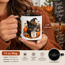 Load image into Gallery viewer, A woman in a rust-brown sweater holds a white ceramic mug with a black handle and interior. The mug features a fall-themed illustration of a black cat in a witch hat with sunflowers and pumpkins.
