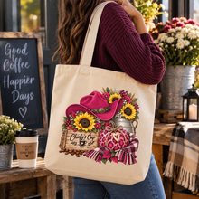 Load image into Gallery viewer, A woman in a burgundy sweater and blue jeans carries a cream canvas tote bag with a colorful western-themed graphic featuring a pink hued cowboy hat, sunflowers, a galvanized bucket, and a pink hued heart-shaped and leopard print pumpkin. The tote bag has the text 'Chiefy's Cup Coffee Co.
