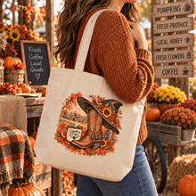 Load image into Gallery viewer, A woman wearing a rust-colored knit sweater and blue jeans carries a cream canvas tote bag with a fall-themed graphic. The graphic features a cowboy boot, a sunflower, a mug that reads 'Chiefy's Cup,' and autumn leaves.
