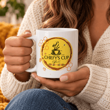 Load image into Gallery viewer, A person in a cream knit sweater holds a white ceramic mug with a circular yellow and brown graphic that reads "CHIEFY'S CUP Coffee Co.".
