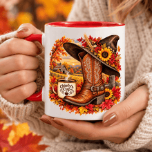 Load image into Gallery viewer, A white ceramic mug with a red handle and interior, held by hands wearing a beige knit sweater. The mug features a detailed autumn-themed graphic with a brown cowboy boot wearing a black hat decorated with sunflowers and red leaves, alongside a small coffee cup labeled 'Chiefy's Cup' and an autumn landscape.

