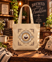 Load image into Gallery viewer, A cream canvas tote bag with a vintage-style coffee cup graphic reading 'Chiefy's Cup Coffee Co. 2020 Premium Coffee' is displayed on a rustic wooden table surrounded by coffee beans, a coffee grinder, a coffee mug, and themed background decor.
