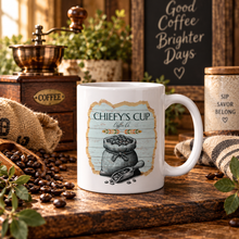 Load image into Gallery viewer, A white ceramic coffee mug with a rustic 'Chiefy's Cup Coffee Co.' graphic, styled on a wooden table with coffee beans, a coffee grinder, and cozy cafe props.
