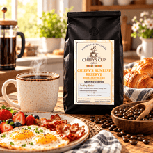 Load image into Gallery viewer, A black bag of Chiefy's Cup Coffee, Chiefy's Sunrise Reserve Breakfast Blend, stands on a rustic wooden table surrounded by a breakfast spread with a cup of coffee, eggs, bacon, strawberries, and croissants.
