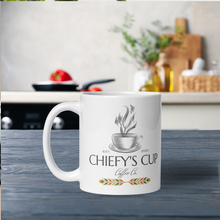 Load image into Gallery viewer, Left side view of white glossy mug featuring the Chiefy’s Cup logo with the image phrase &quot;Chiefy’s Cup,&quot; showing a black cup and saucer with black steam rising from the cup.
