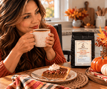Load image into Gallery viewer, A woman in a rust-colored sweater holds a mug at a wooden table, with a bag of Chiefy's Cup Autumn Pecan Delight Arabica coffee standing nearby. A pecan pie with whipped cream sits on a plate in front of her, and autumn decorations including pumpkins and fall leaves decorate the table.
