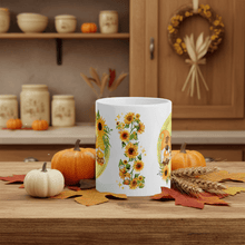 Load image into Gallery viewer, White mug with sunflower design on a wooden table with pumpkins and fall leaves.
