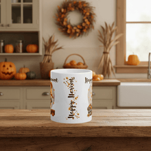 Load image into Gallery viewer, White mug with &#39;Happy Harvest&#39; design on a wooden table in a kitchen decorated for fall.
