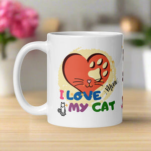 Left side view of a white glossy mug with a red heart design featuring a cat nose and whiskers in the center. Behind the heart is a faded yellow circle. The words “I love my cat” are displayed, along with a tiny cat outline and the playful word “meow.”