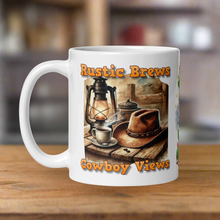 Load image into Gallery viewer, Left side view 11 oz white glossy mug with image phrase &quot;Rustic Brews Cowboy Views,&quot; featuring a rustic cowboy hat resting on a weathered table, with a steaming cup of coffee and an old lantern beside it.
