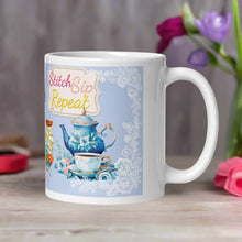 Load image into Gallery viewer, Right side view white glossy mug with the phrase &quot;Stitch Sip Repeat,&quot; featuring a vintage coffee pot with a cup and saucer, set against a light blue background and lace frame.
