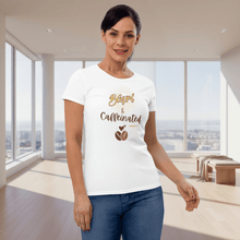 Load image into Gallery viewer, Front view of a woman wearing a white “Blessed &amp; Caffeinated” t-shirt featuring gold and brown lettering with a coffee bean graphic. The bright modern indoor setting gives a clean, fresh, and uplifting feel.

