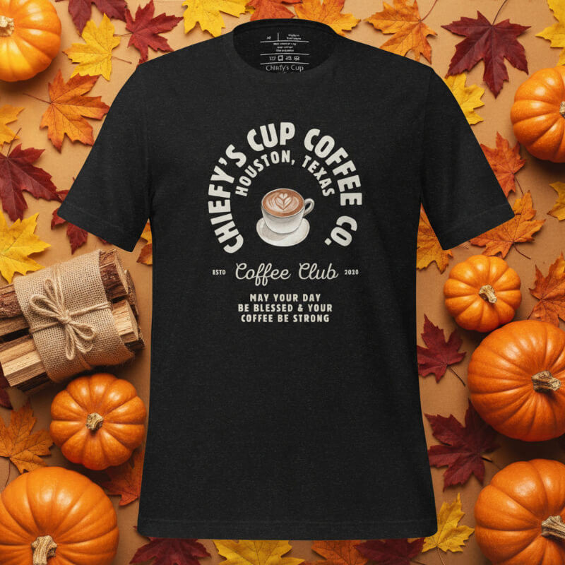 Black t-shirt with coffee-themed design on a background of pumpkins and autumn leaves