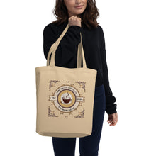 Load image into Gallery viewer, Person holding a beige tote bag with text and a circular design on a white background
