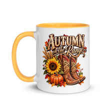 Load image into Gallery viewer, A white ceramic coffee mug with a yellow handle and interior, featuring a graphic design that reads 'AUTUMN on the Range' in rustic lettering, surrounded by a fall harvest illustration with a sunflower, pumpkins, and cowboy boots.
