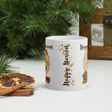Load image into Gallery viewer, Back side view of a white ceramic mug showcasing the phrase &quot;Happy Harvest&quot; with a design of blowing leaves, sunflowers, small acorns, and mushrooms.
