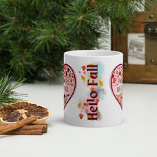 Load image into Gallery viewer, Back side view of a white glossy mug with the phrase &quot;Hello Fall,&quot; set against autumn-colored hues with blowing leaves in the background.
