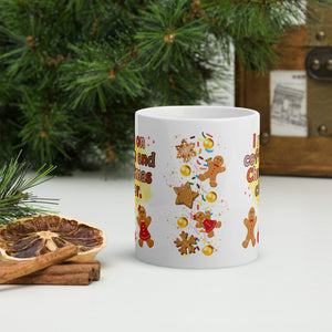 Back side view of a white glossy mug with gingerbread cookies, cookie sprinkles, golden sparkles, and large yellow cookie decorations in the background.