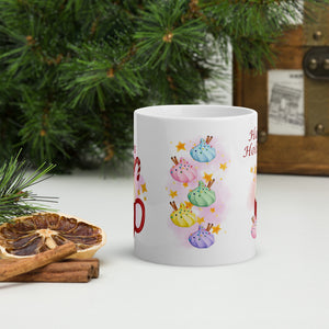 Back side view of a white glossy mug with colorful puff pastries topped with sprinkles and cinnamon sticks, accented by golden stars and a pink-hued background.