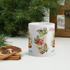 Back side view of a white glossy mug with a design of Christmas ornaments, mistletoe, pine trimmings, cocoa cups topped with candy canes and cookies, with golden sparkles and light yellow hues in the background.