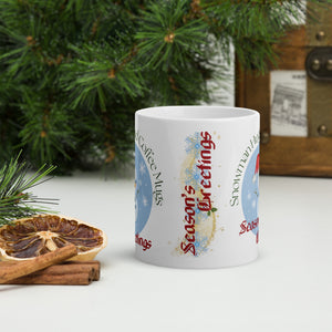 Back side view of white glossy mug with the phrase "Season's Greetings" in festive font, showcasing bright blue and gold snowflakes, golden sparkles, and small holly accents.