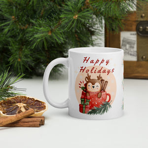 Left side view of a white glossy mug with the phrase "Happy Holidays" in festive font, featuring a baby reindeer inside a mug, red Christmas present, pine tree trimmings, snowflakes, and golden sparkles.