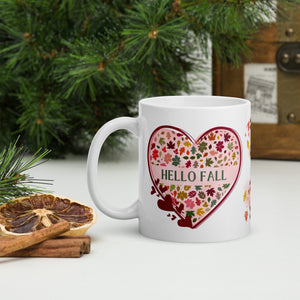 Left side view of a white glossy mug with the phrase "Hello Fall," featuring a heart-shaped leaf design, a red heart-shaped frame, and a pink-hued heart-shaped background.