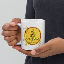 Load image into Gallery viewer, A person holding a white ceramic coffee mug with a gold and brown circular graphic that reads 'CHIEFY'S CUP Coffee Co'. The person is wearing a dark gray t-shirt against a light gray background.
