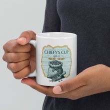 Load image into Gallery viewer, A person holding a white ceramic coffee mug with a vintage-style illustration of a sack of coffee beans and the text 'CHIEFY'S CUP Coffee Co.' The person is wearing a dark gray t-shirt against a light gray background.
